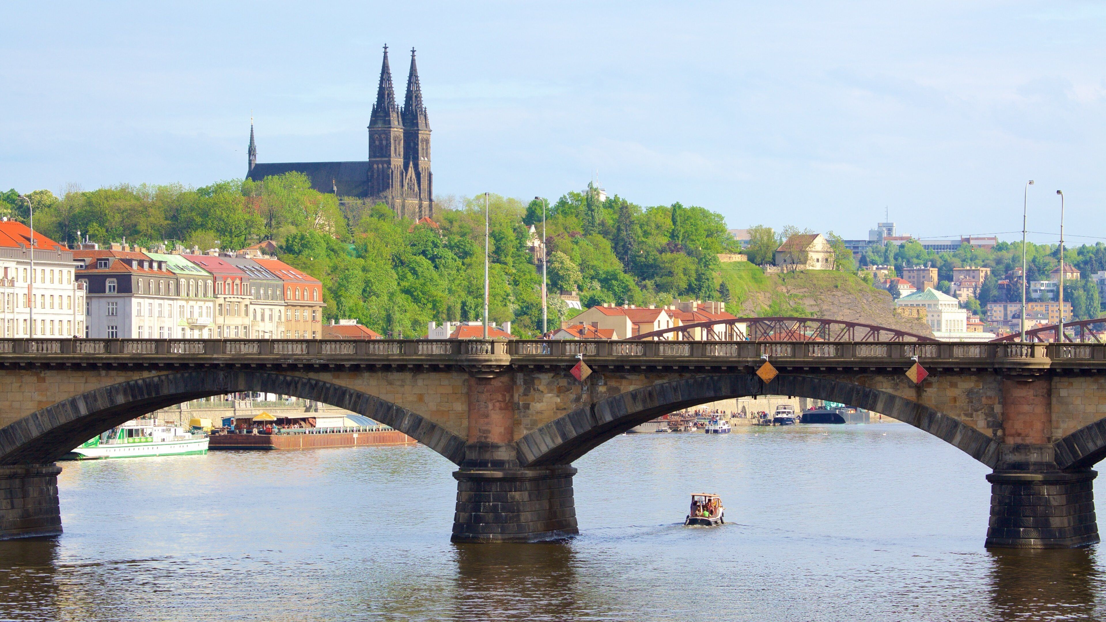 A stone bridge over a river with a boat in the foreground and a cathedral in the background.