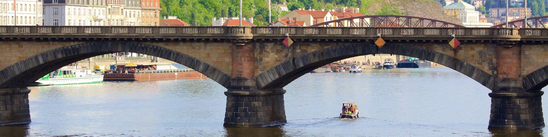 A stone bridge over a river with a boat in the foreground and a cathedral in the background.