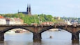 A stone bridge over a river with a boat in the foreground and a cathedral in the background.