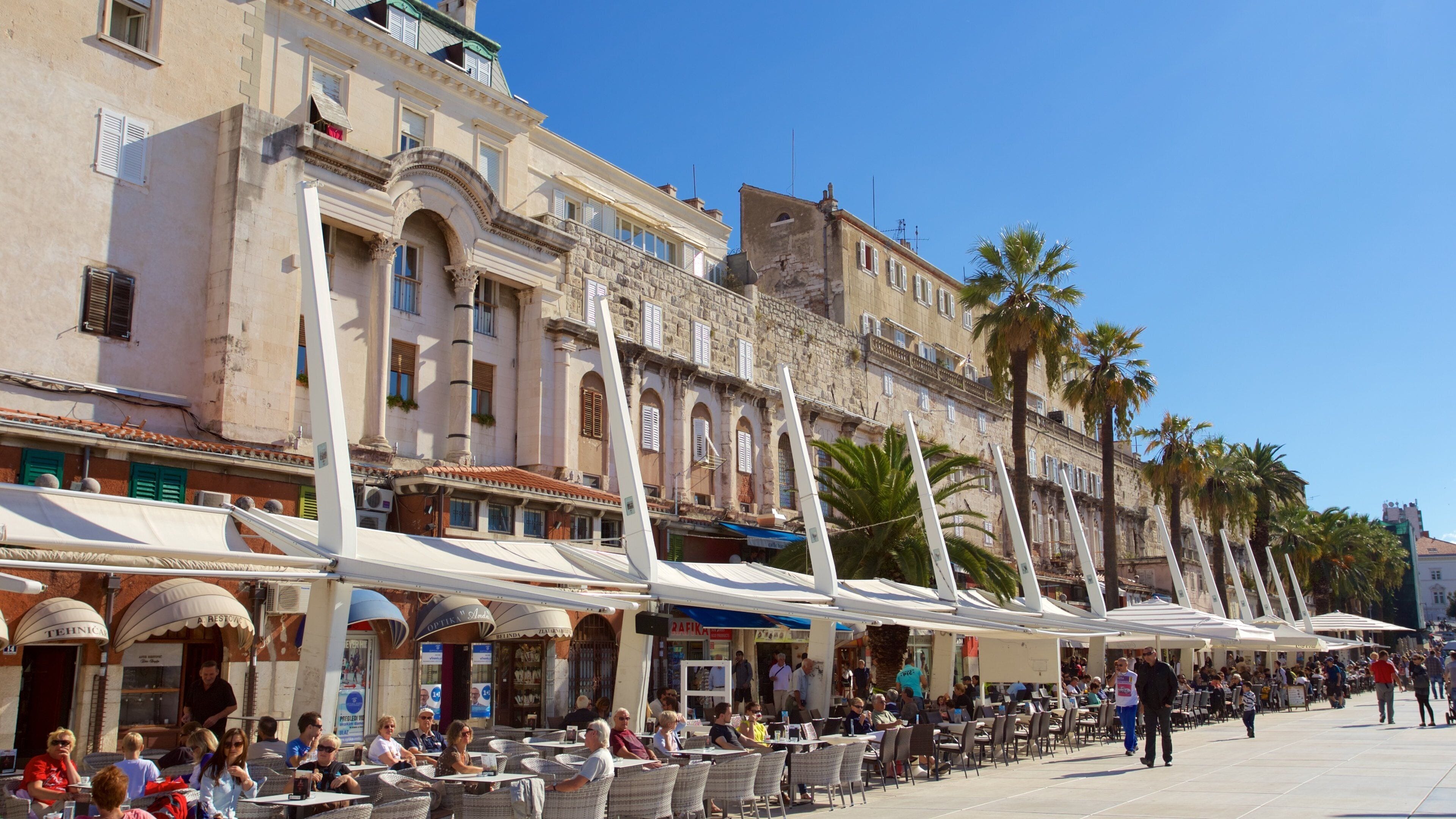 A bustling outdoor café area with outdoor seating and palm trees.