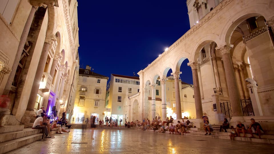 A historic square with classical architecture, including arches and columns, and a crowd of people.