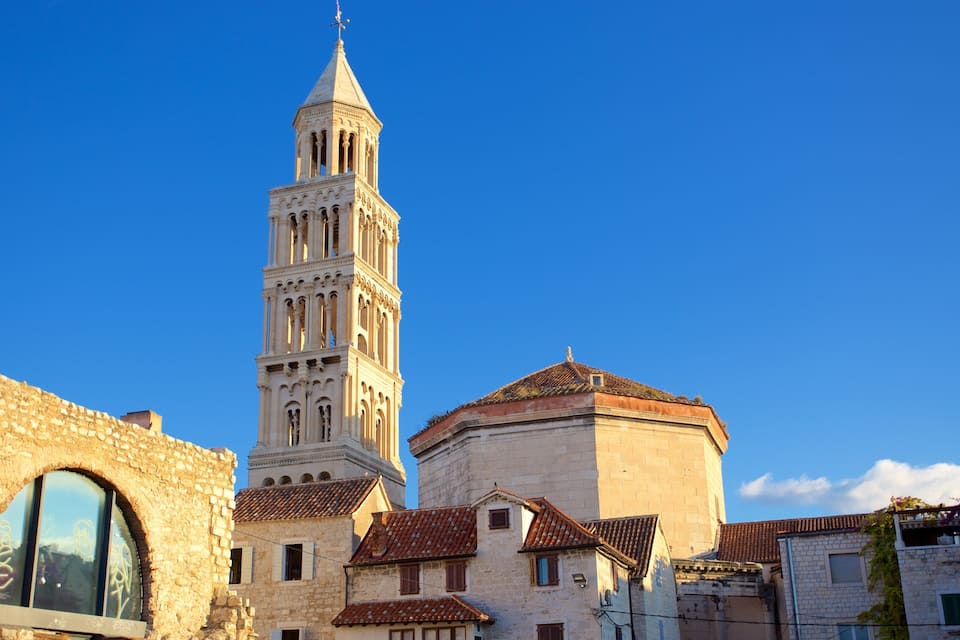 Una torre storica con una campana, un edificio in pietra con una cupola e un cielo azzurro limpido.