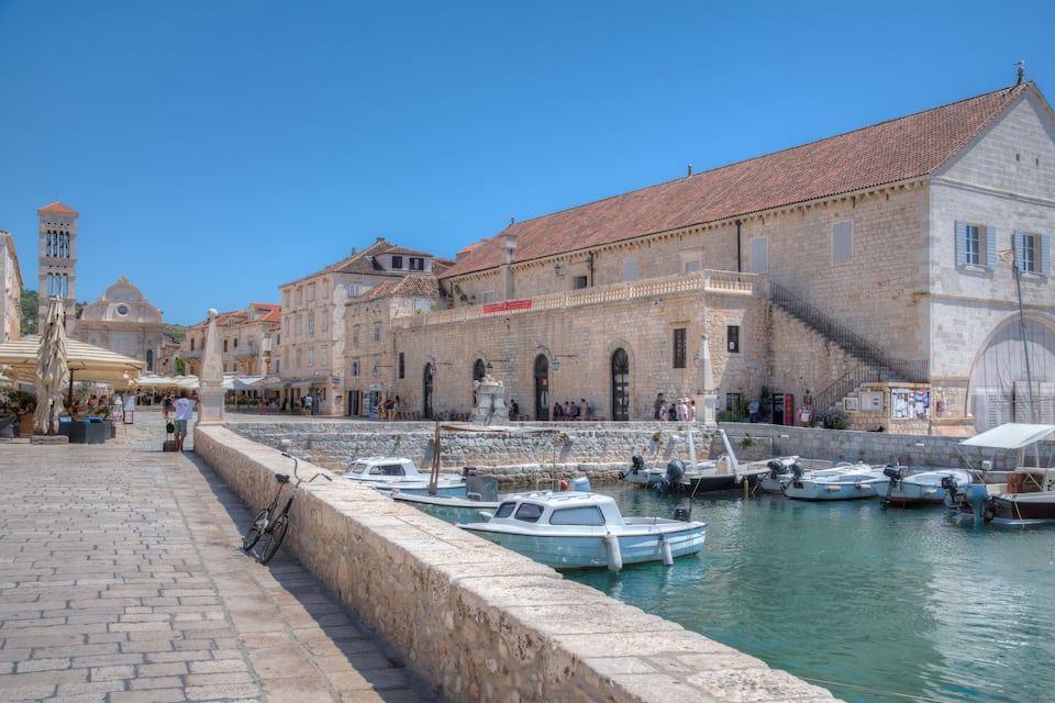 Un muelle histórico con edificios de piedra, una torre del reloj y barcos amarrados a lo largo del dique.