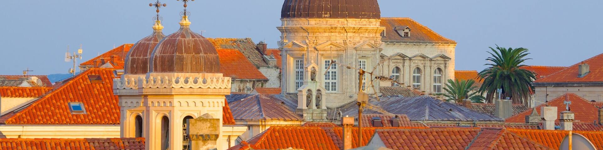 A historic building with a large dome and a smaller dome with a cross on top, surrounded by red-tiled roofs.