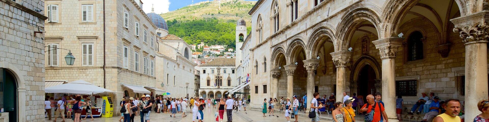 Una plaza histórica con edificios de piedra, arcos y una colina al fondo.