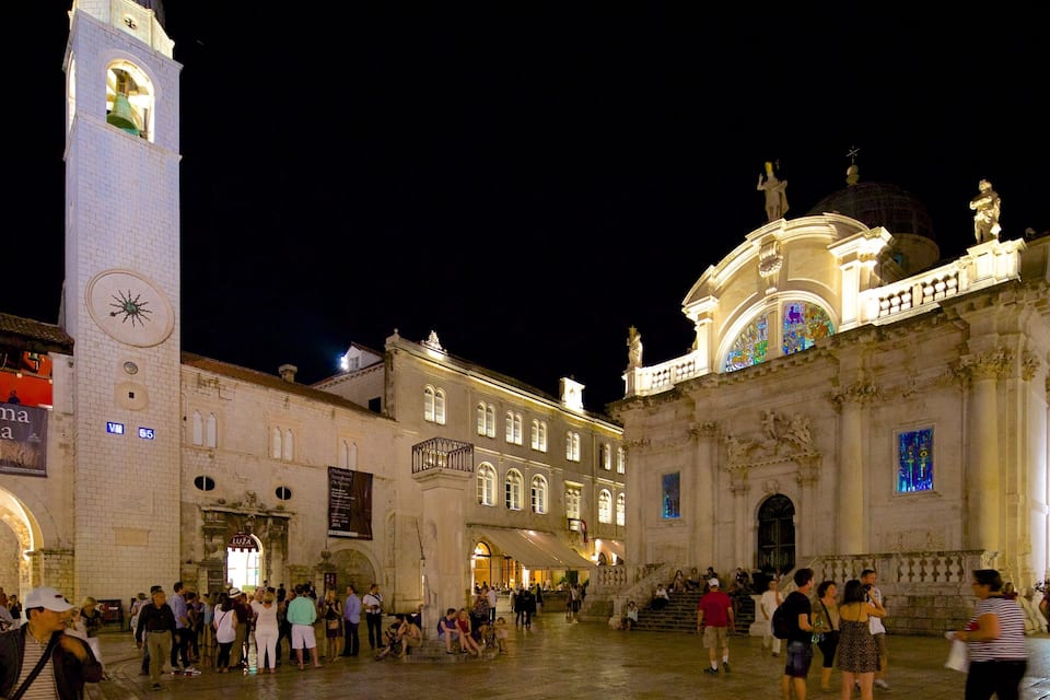 Una plaza histórica con una imponente torre del reloj y un edificio grande de cúpula.