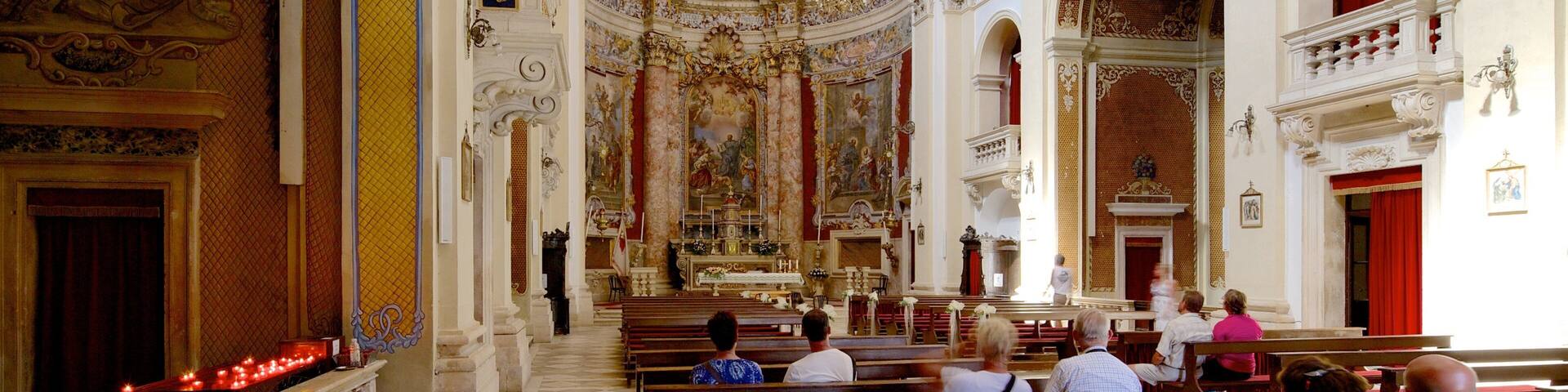 An ornate church interior with high ceilings, detailed frescoes, and red curtains.