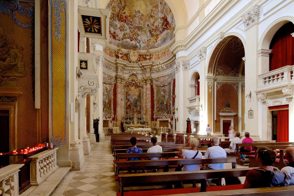 An ornate church interior with high ceilings, detailed frescoes, and red curtains.
