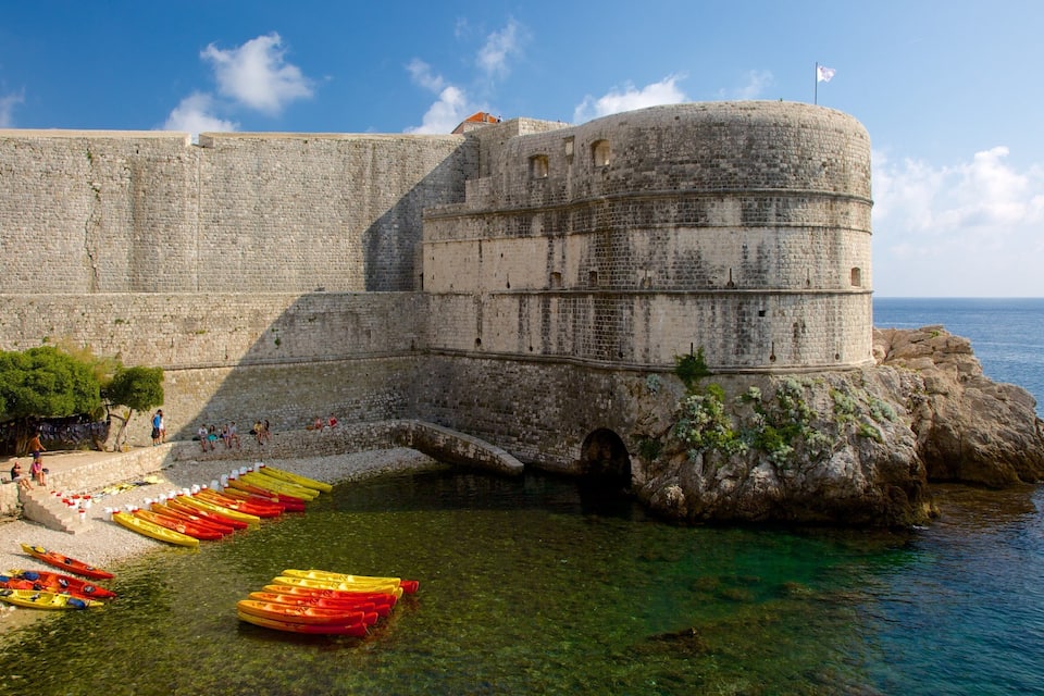 Een historiek stenen fort aan zee, met helder water en kleurrijke kajaks langs de kust.