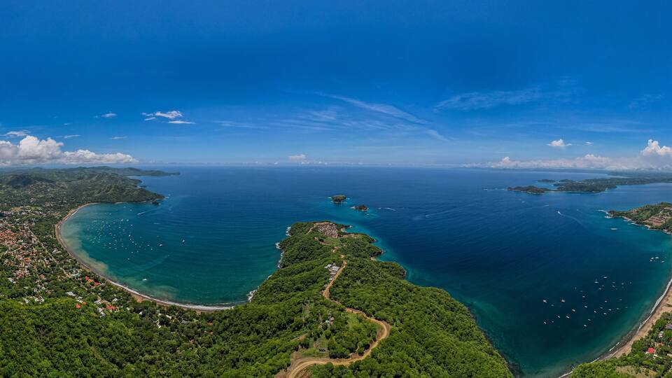 A coastal landscape with a bay, green hills, and a clear blue sky.