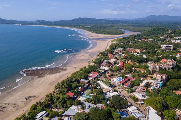 Eine Küstenstadt mit Strand, Häusern und Bergen im Hintergrund.