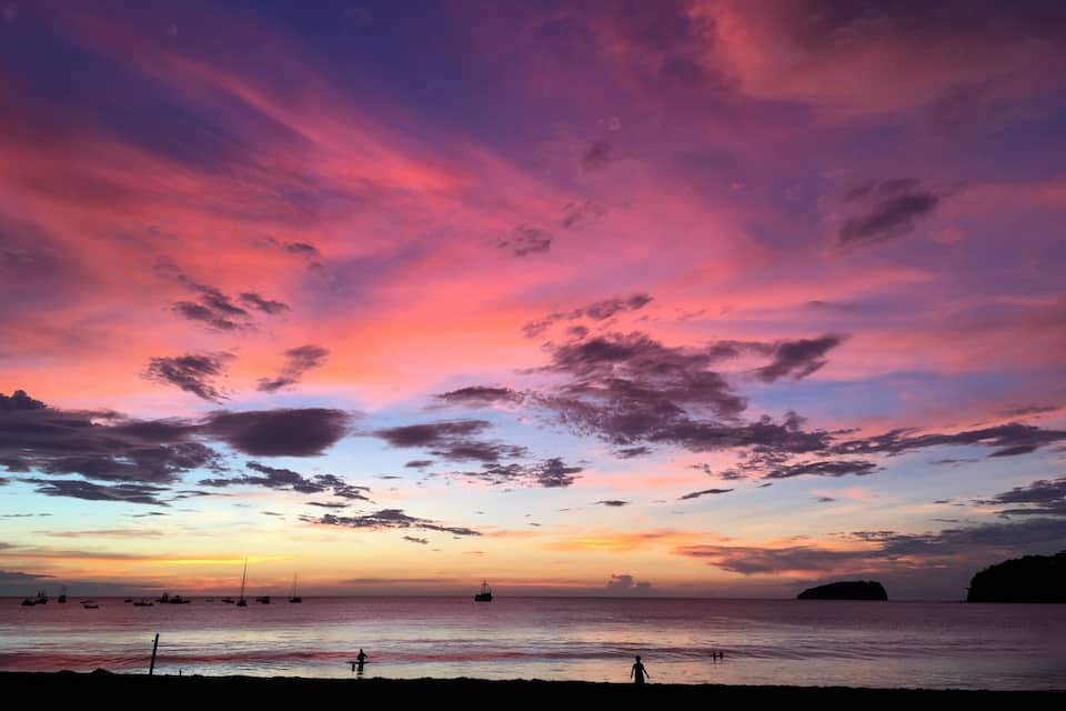 Un coucher de soleil sur l’océan, avec des bateaux et la silhouette d’une masse terrestre.