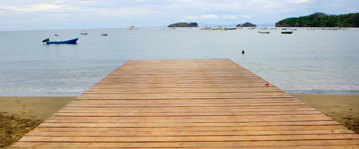 A wooden pier extending into calm waters with boats and small islands in the distance.