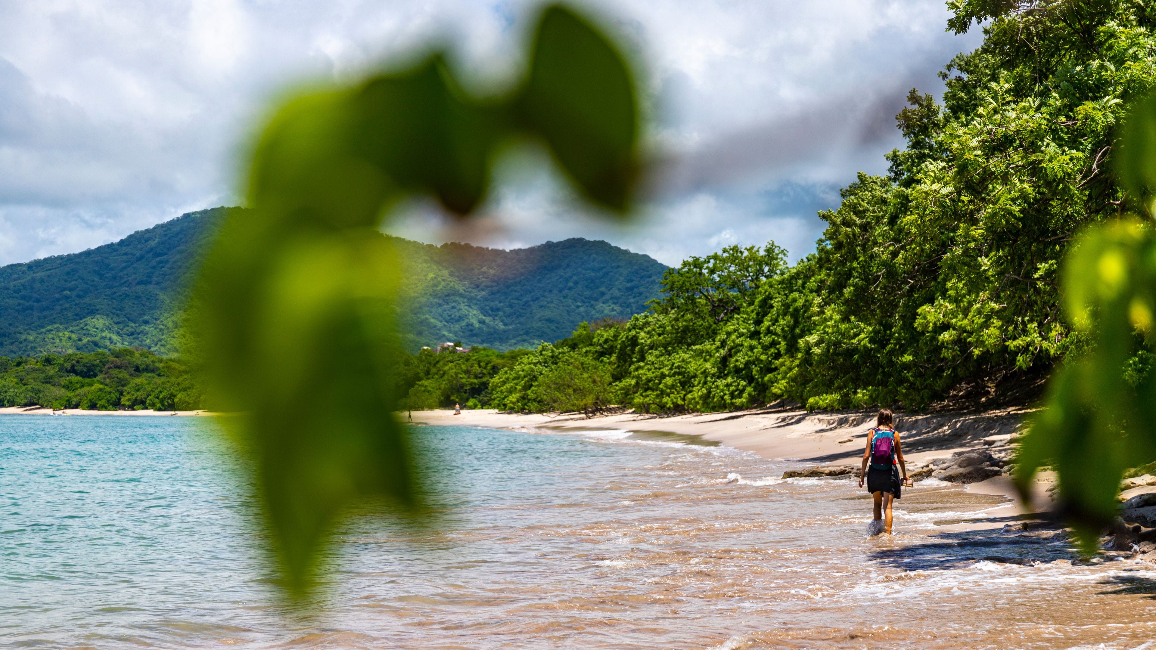 a beautiful girl in a short skirt walks on the famous conchal beach on the pacific coast of Costa Rica; a paradise beach with turquoise water and green hills in the background