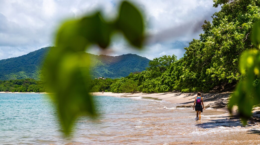 a beautiful girl in a short skirt walks on the famous conchal beach on the pacific coast of Costa Rica; a paradise beach with turquoise water and green hills in the background