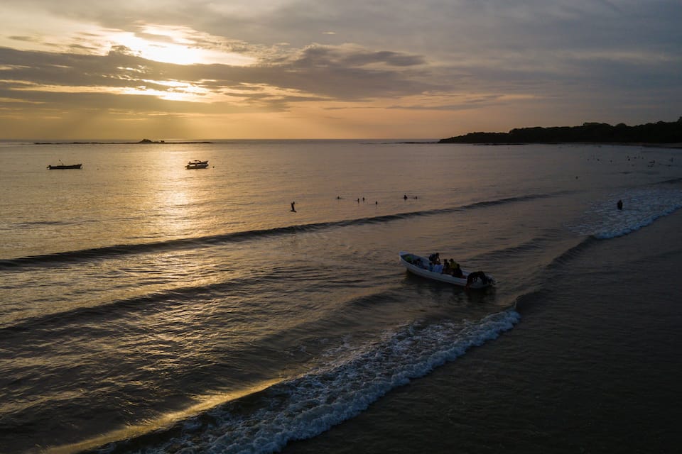 A sunset over a beach with a boat and people in the water.