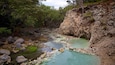 A clear stream with rocky banks and surrounding greenery.