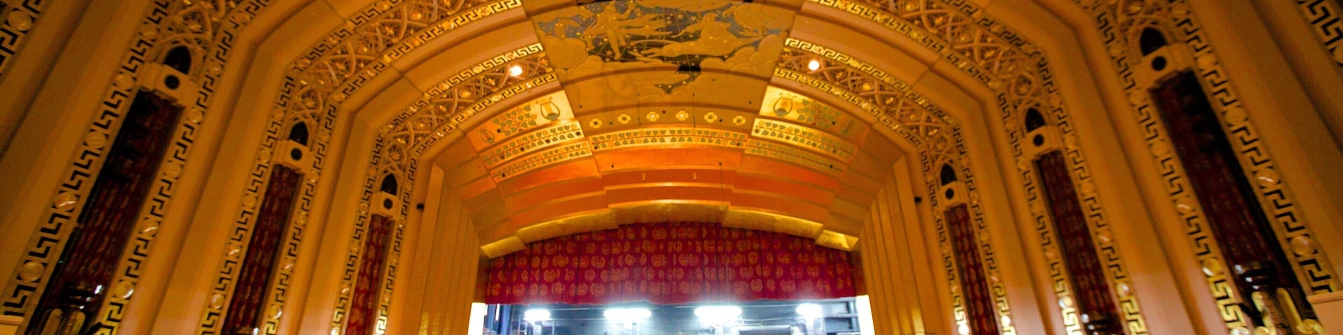 Interior de teatro ornamentado com designs elaborados no teto e palco.