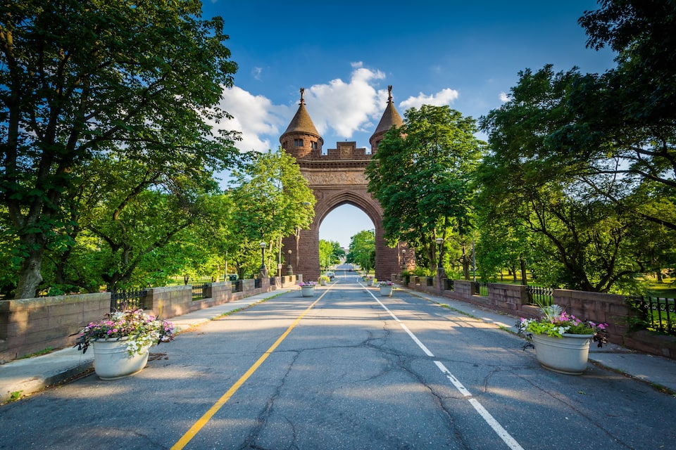 A historic stone bridge with two towers, surrounded by lush green trees and flower pots along the pathway.