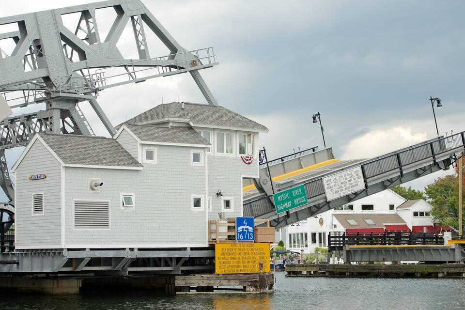 A drawbridge over Mystic River, a white building labeled 'Mystic River Inn', and a sign indicating the bridge's clearance height.