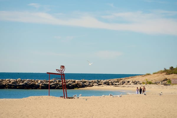 A beach with a red metal chair, rocky shoreline, and people walking.