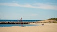 Una spiaggia con una sedia di metallo rossa, un litorale roccioso e persone che passeggiano.