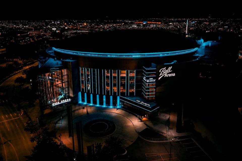 A brightly lit building with a circular design, surrounded by a parking area and a cityscape in the background.