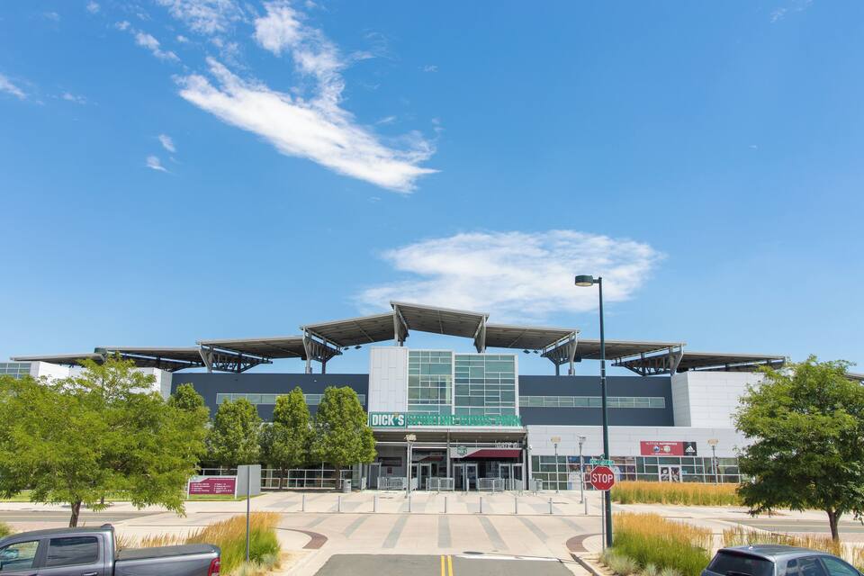 A modern sports complex with a large stadium, covered walkways, and a parking area.