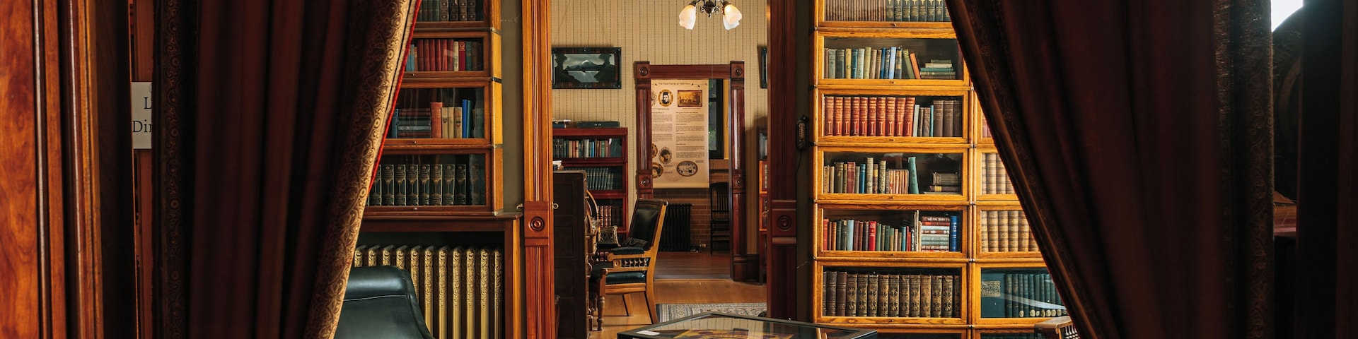 Une bibliothèque avec des étagères en bois, une table recouverte de velours rouge, un fauteuil en cuir et un lustre.