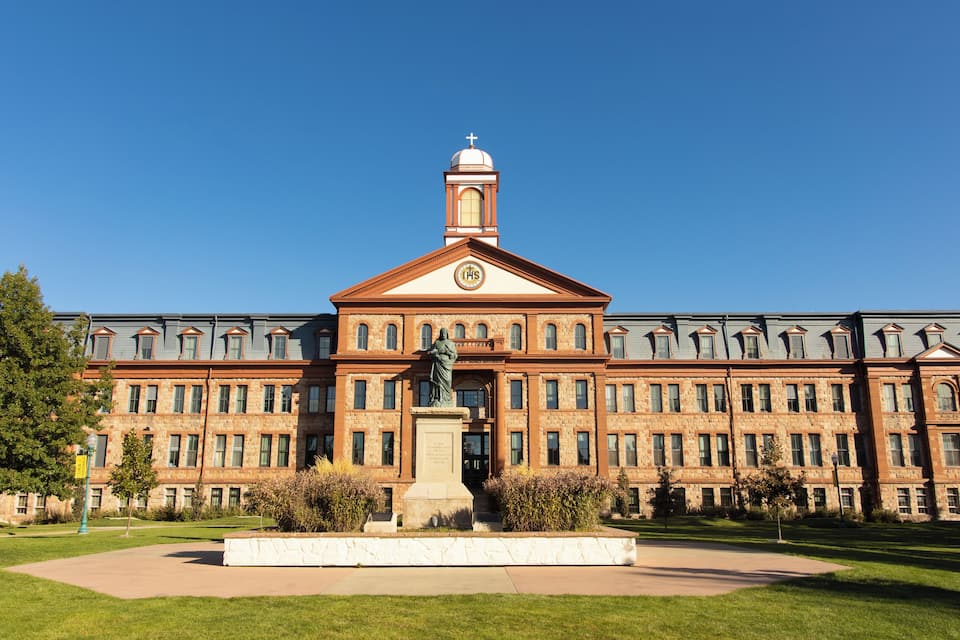 A large, historic building with a prominent clock tower and a statue in front.