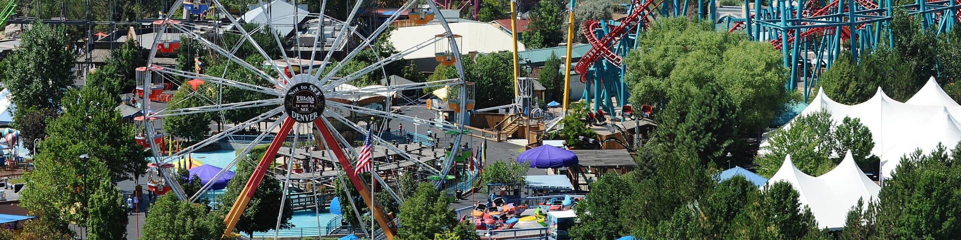 Visitors enjoy thrilling rides at Elitch Gardens Theme Park in Denver, Colorado, with city skyline and mountains in the background