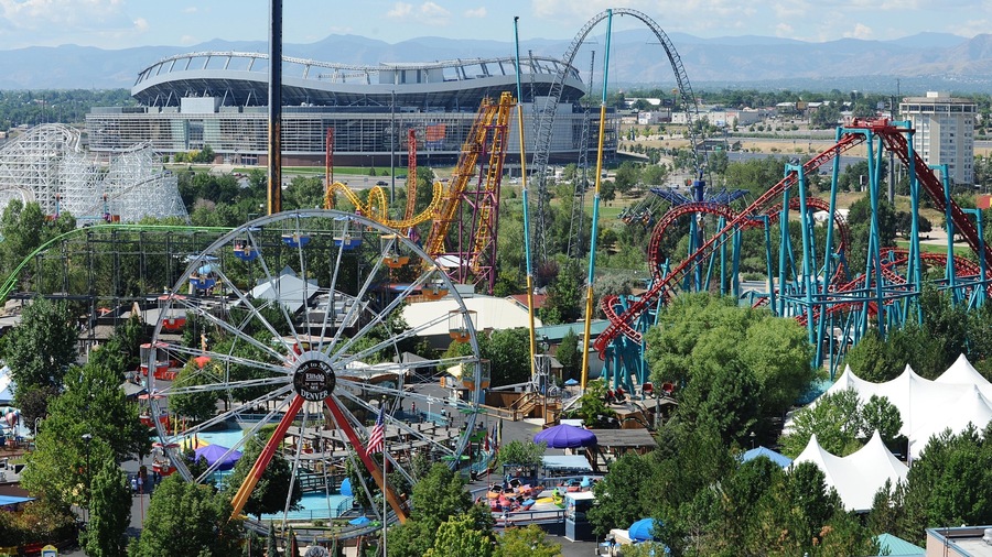 Visitors enjoy thrilling rides at Elitch Gardens Theme Park in Denver, Colorado, with city skyline and mountains in the background
