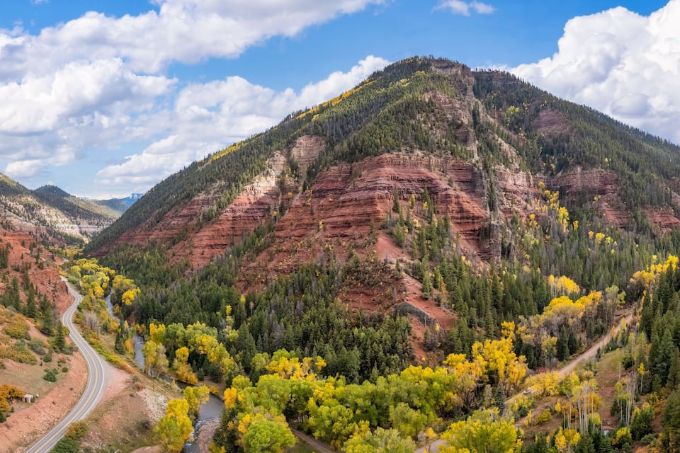 A mountain landscape with a winding road, dense forests, and a river.