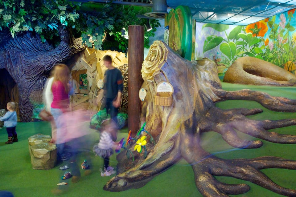 Escultura grande de árvore com raízes e um cesto em uma área de recreação infantil.