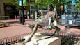 A statue of a woman in a dress sitting on a bench in a public square.
