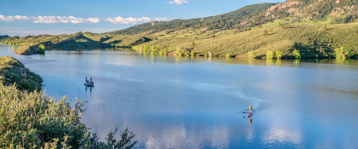 summer morning on  Horsetooth Reservoir at foothills of Rocky Mountains in northern Colorado with a fishing boat and a stand up paddler, popular recreation destination in Fort Collins area
