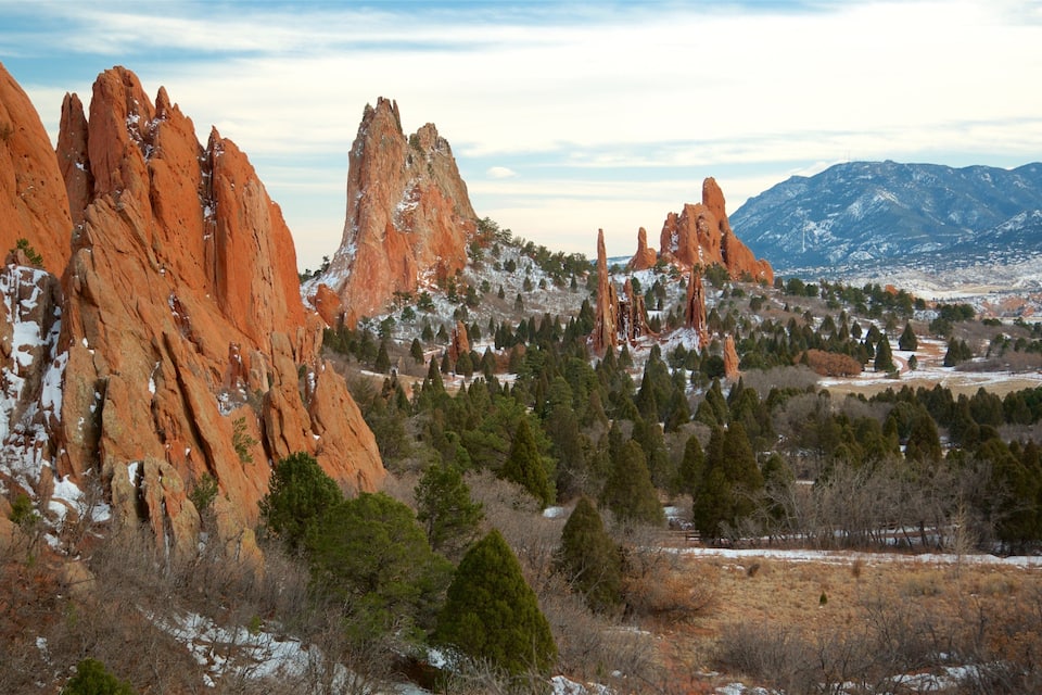 A landscape with red rock formations, snow patches, and a distant mountain range.