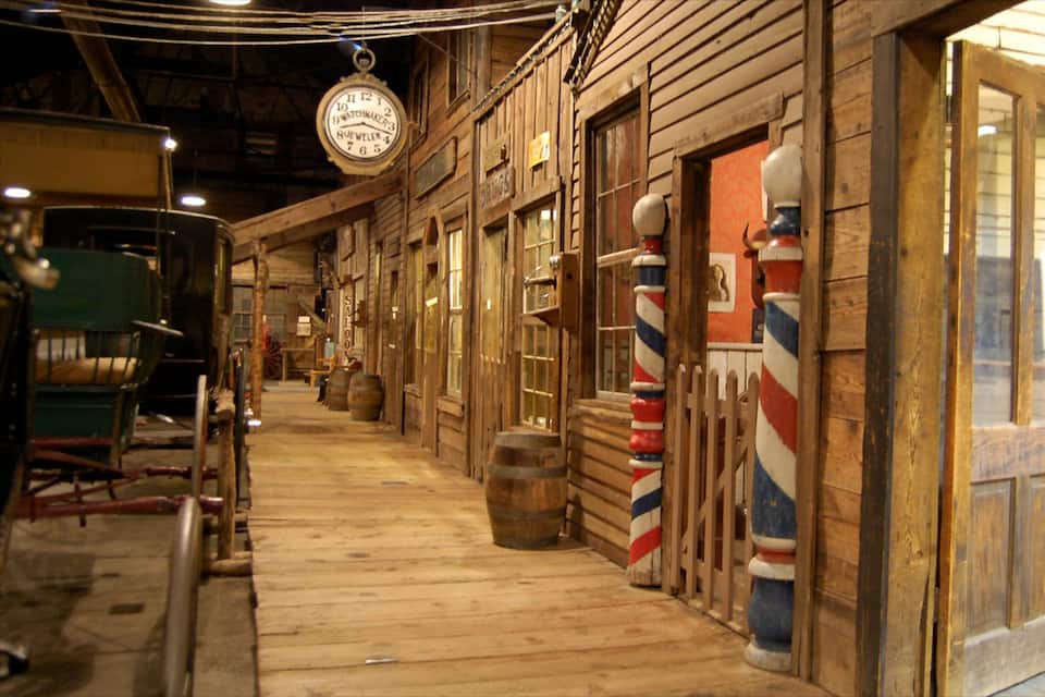 Un edificio de madera con un reloj, barriles y un llamador de barbero.