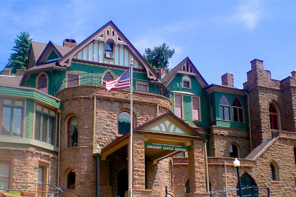 Edificio histórico con fachada verde, torre de piedra y bandera estadounidense.