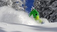A person snowboarding down a snowy slope with trees in the background.