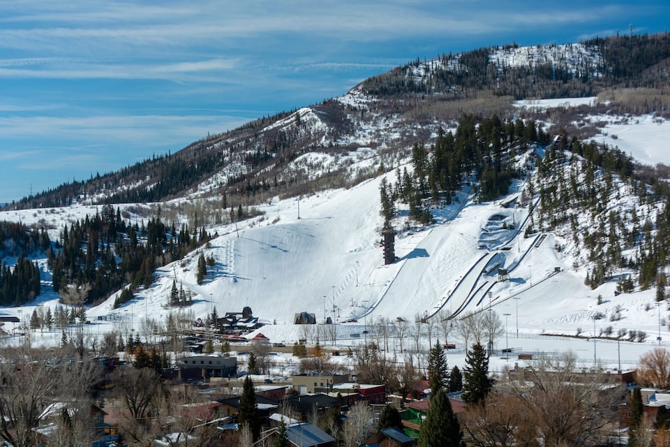A snow-covered mountain with ski slopes, a small town at the base, and a clear blue sky.