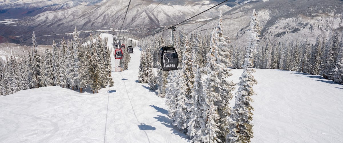 A ski lift in a snowy mountain landscape with snow-covered trees and distant mountains.