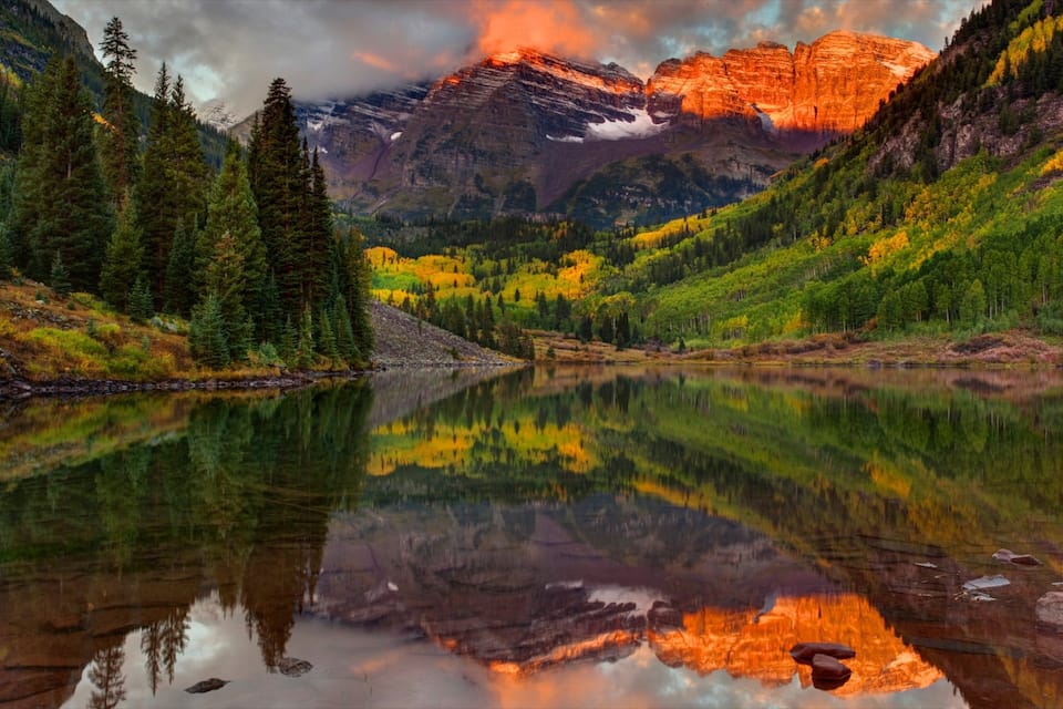 A mountain lake with reflections, surrounded by autumn-colored trees and a prominent mountain in the background.