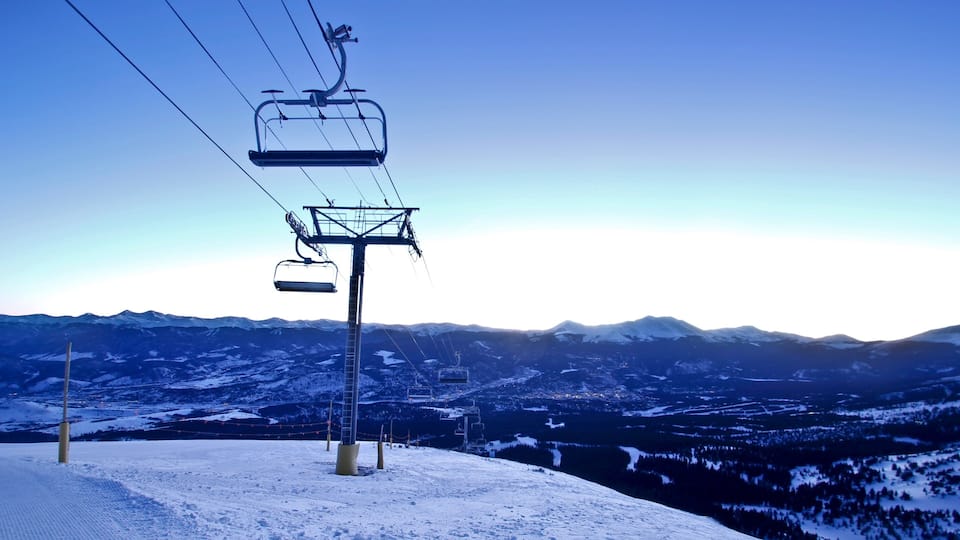 A ski lift with cables against a snowy mountain backdrop.
