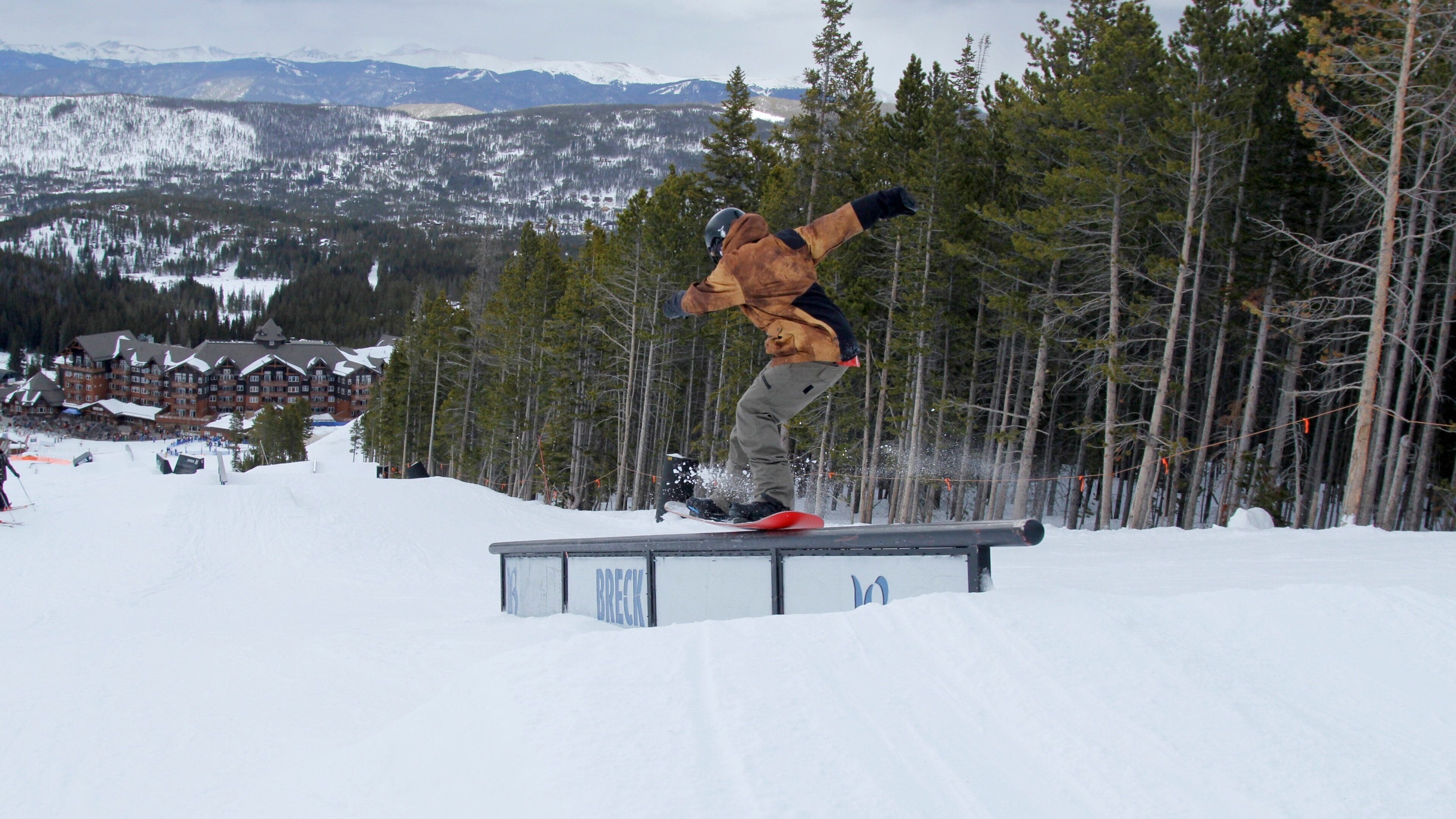 A snowboarder performing a trick on a rail in a snowy mountain setting.
