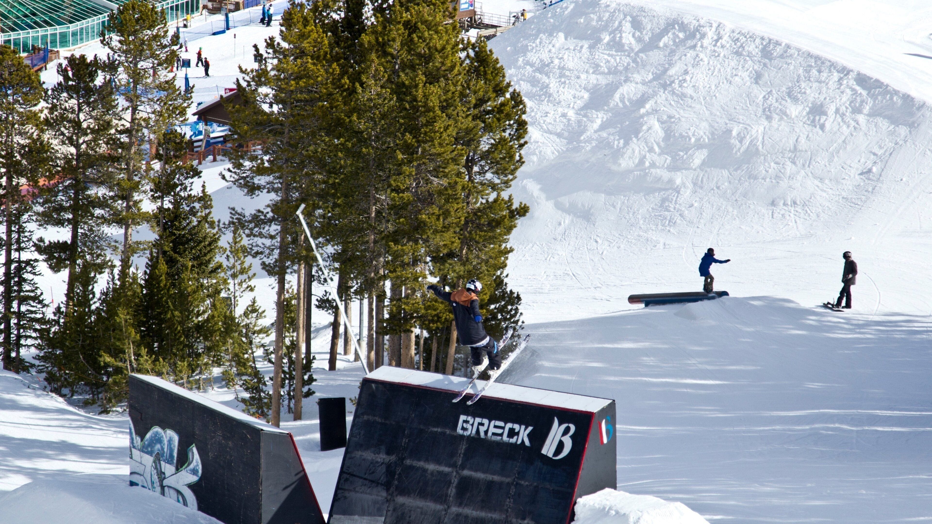 A snow-covered ski slope with a wooden structure labeled "GRECK 18" and a person snowboarding.