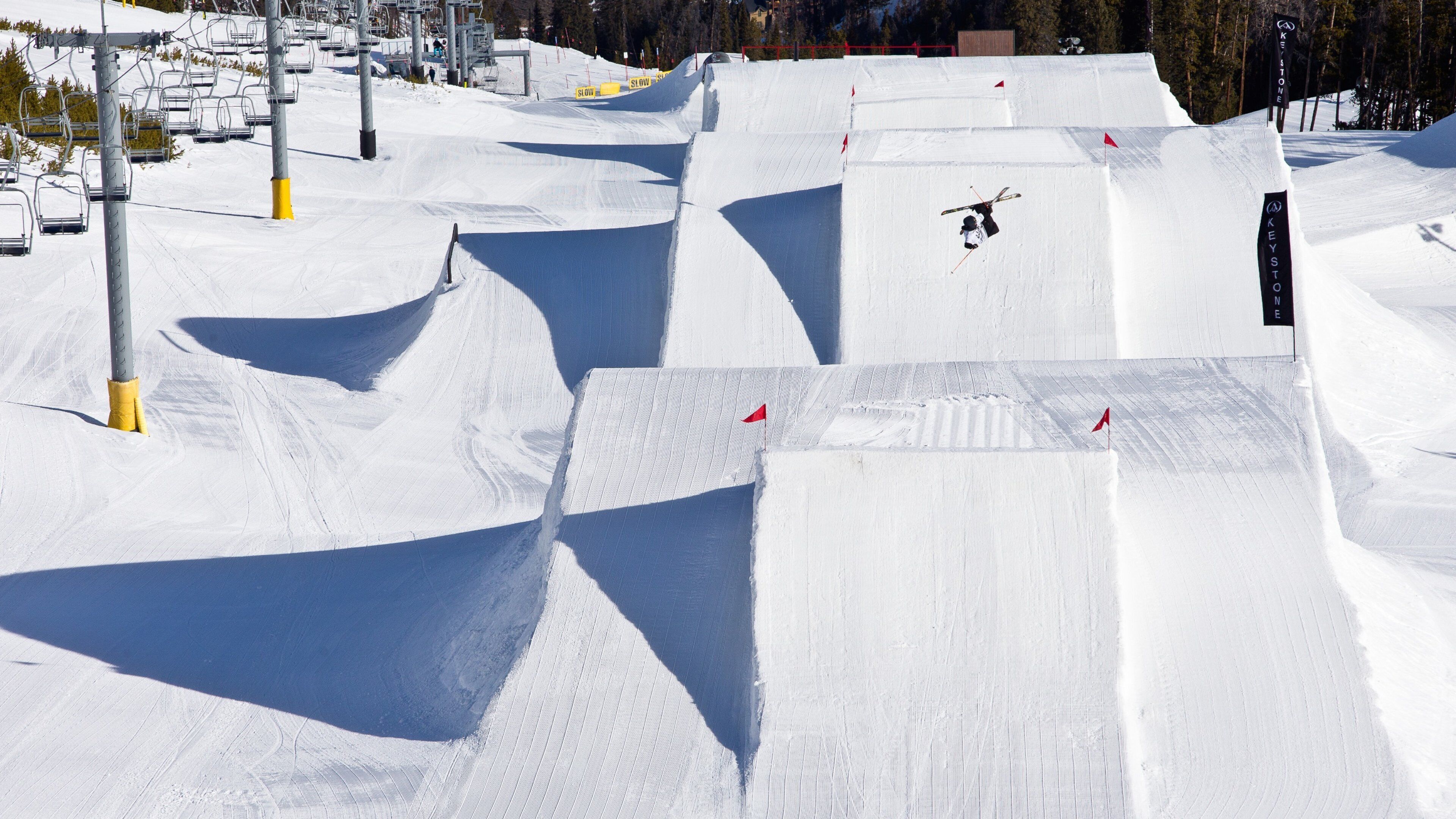 Pista de esquí nevada con varios saltos y un telesilla al fondo.