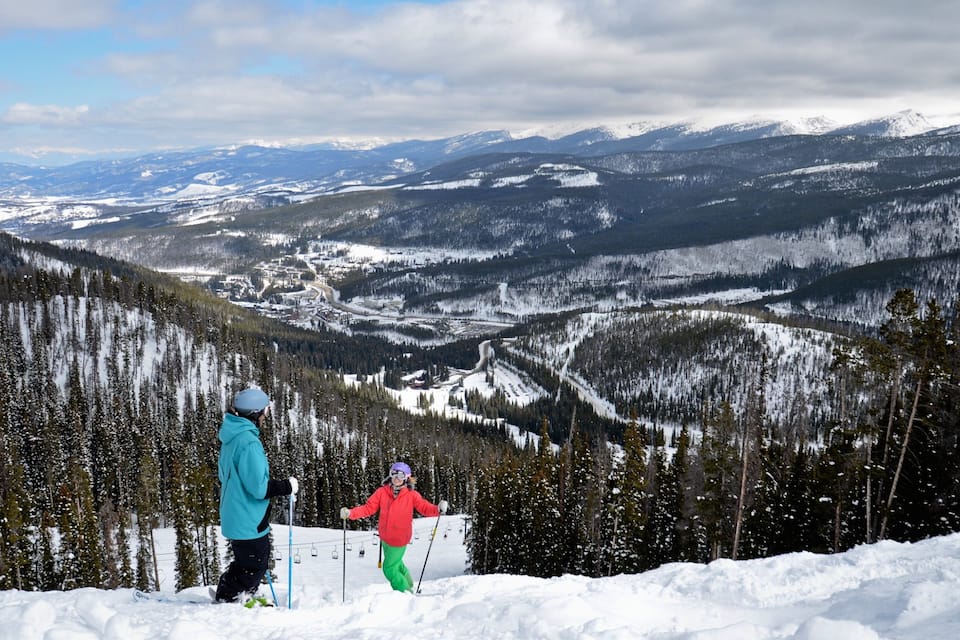 Un paysage montagneux enneigé avec des pistes de ski, un télésiège et une ville située dans la vallée.
