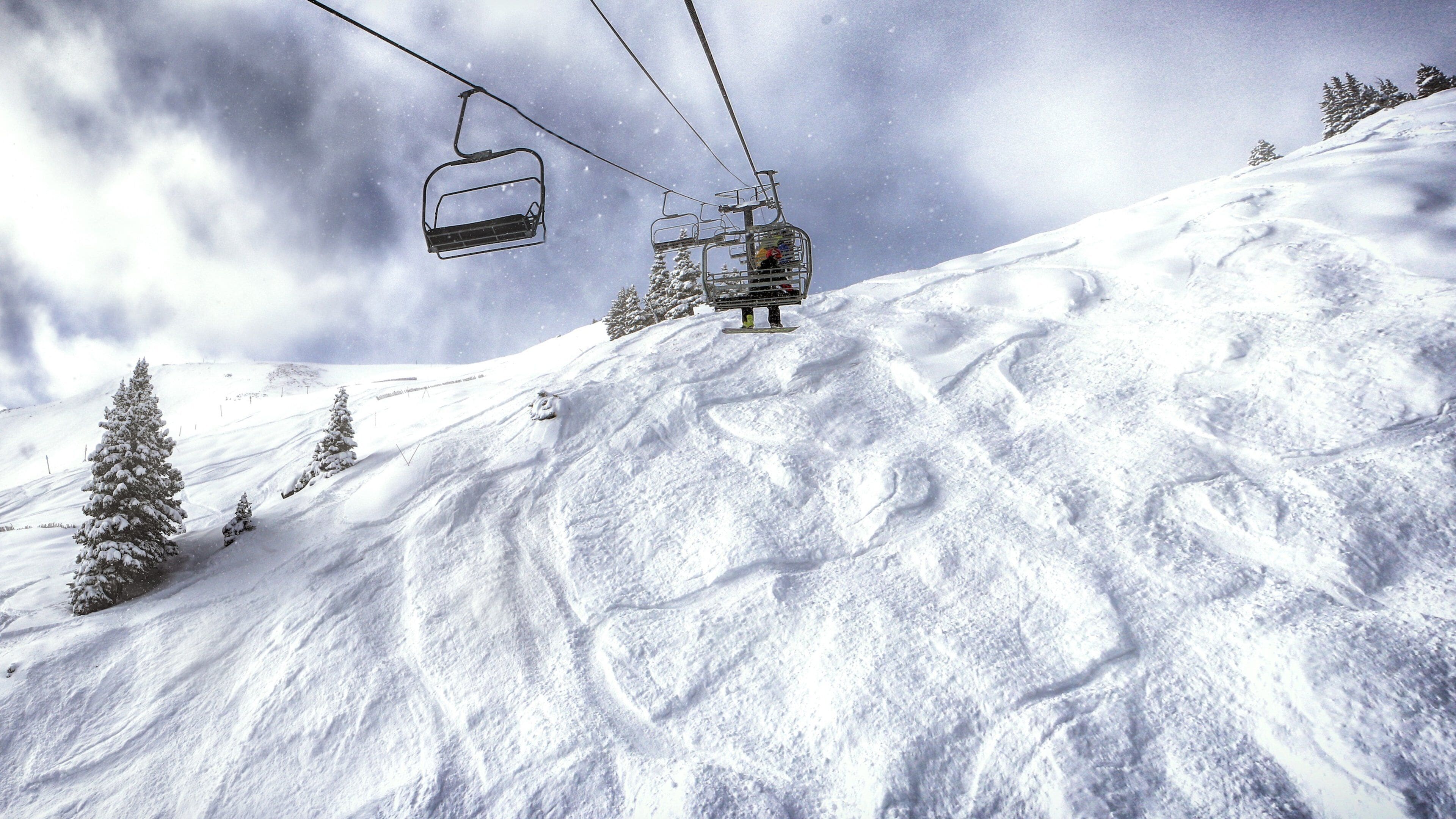 A ski lift chair suspended over a snowy mountain slope with tracks and snow-covered trees.