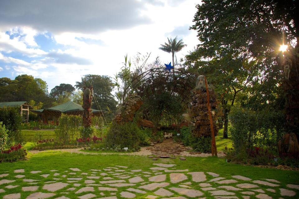 Um jardim com caminhos de pedra, plantas tropicais e um gazebo.